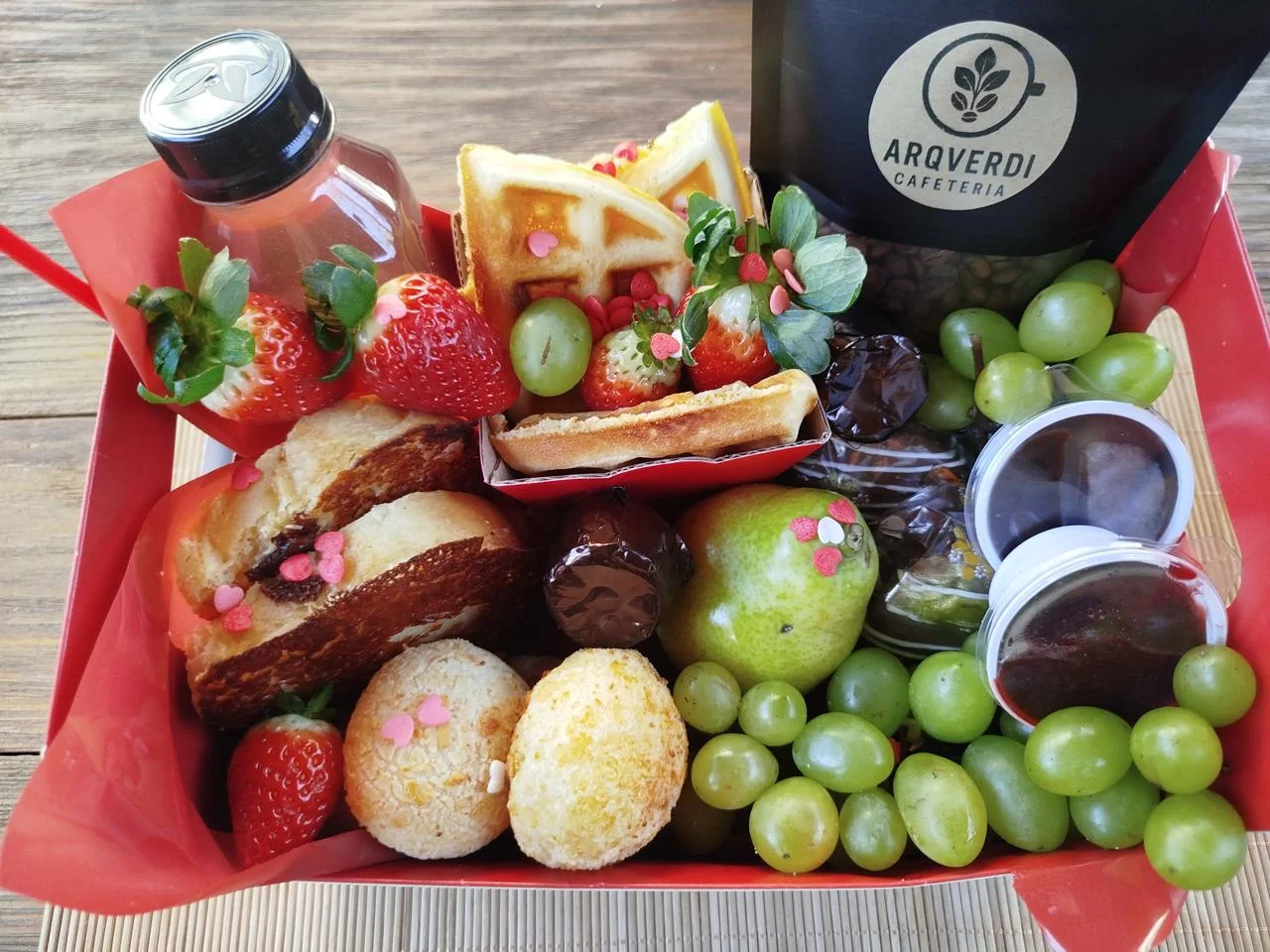 Detalhe de uma cesta de café da manhã com waffles, frutas, pães, doces e café da ArqVerdi.